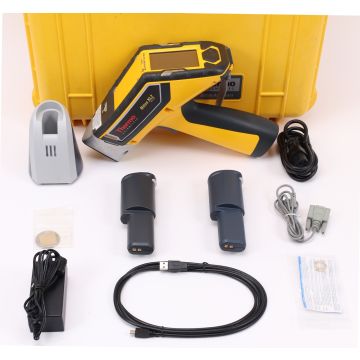 Image of a handheld Niton XL2 980 X-ray fluorescence (XRF) analyzer. The device is gray with black accents and features a digital display screen and various buttons and controls. The user is holding the device in their hand, with the XRF sensor pointed to